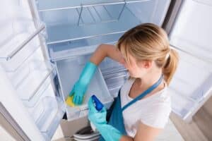 Frau reinigt den Kühlschrank mit Putzutensilien